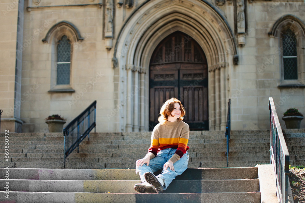 Pretty teen girl sitting on cathedral steps, backlit.