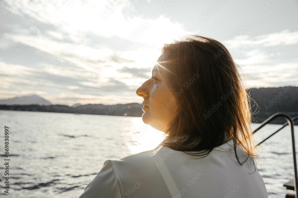 A woman in a yellow dress sits on a causeway by a lake at sunset