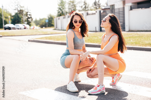 Two young beautiful smiling female in trendy summer cycling shorts  top clothes. Sexy carefree women posing in street at sunny day. Positive models having fun. Cheerful and happy. In sunglasses