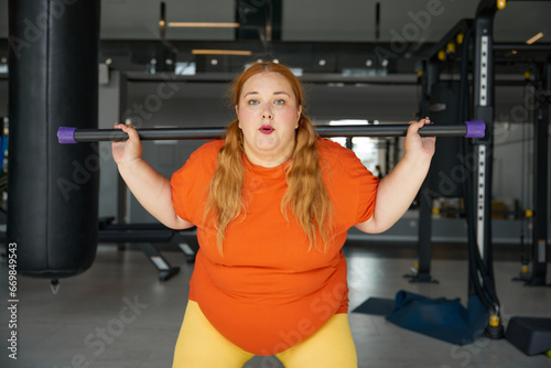 Overweight woman having fitness workout squatting with body bar training equipment