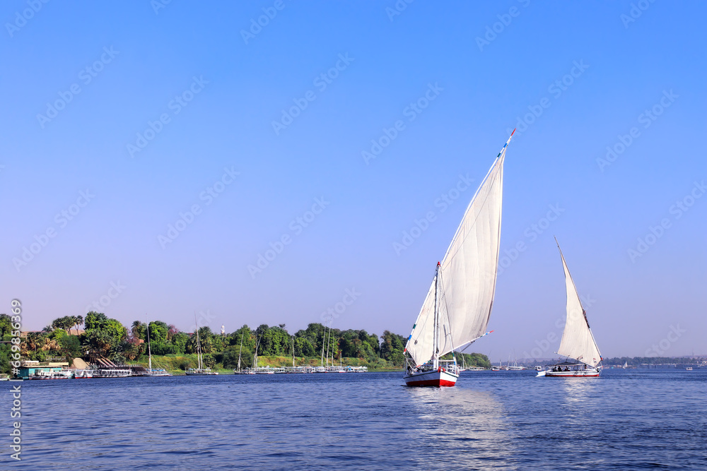 Obraz premium Traditional sailing boat felucca, Nile river near Aswan, Egypt. A famous tourist attraction - sailing boat ride