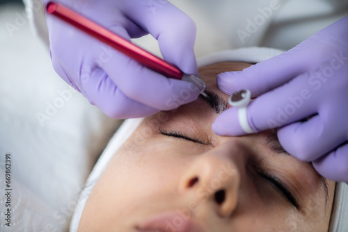 Beautician microblading eyebrows. Professional eyebrow microblading at beauty salon.