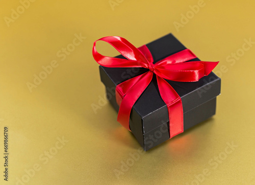 Black gift box with red ribbon on golden background with copy space