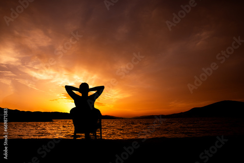 sylwetka osoby o zachodzie słońca siedząca i podziwiająca zachód słońca, relaks nad morzem