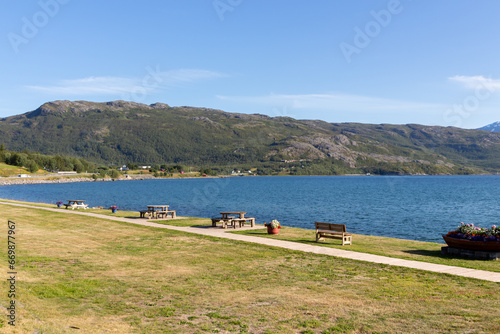Brown wooden benches on the shore of a lake with green mountains in the background