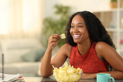 Happy black woman eating potato chips at home photo