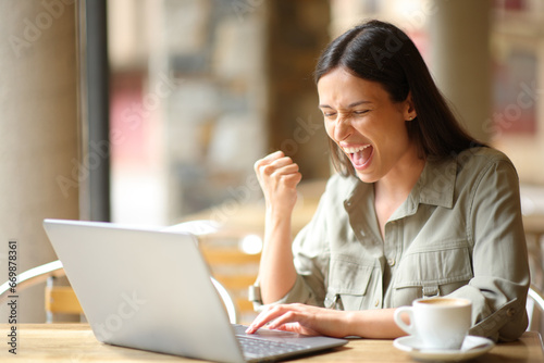 Excited woman celebrating in a restaurant checking laptop