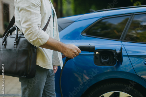 Close up of businessman charging his electric car in front of house. Pluging charger in charging port. © Halfpoint
