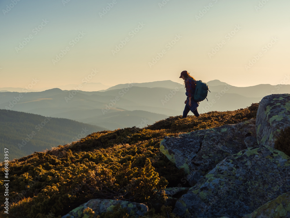 Descent of hiker tourist woman with backpack during mountain trekking from the top.