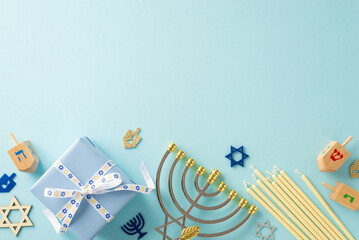 Jewish Tradition: Overhead view of menorah, Star of David symbols, gift box with bow, candles, and dreidel on a soft blue surface—ideal for your text or advertisement