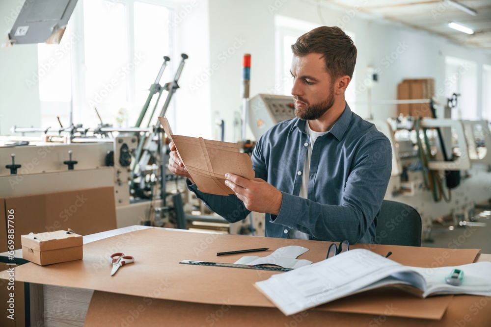 Sitting by the table. Handsome man is working at the factory of creating eco boxes