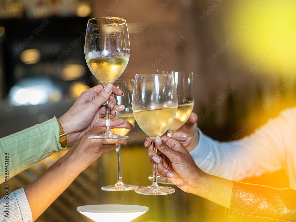 A close-up of friends raising their glasses in a toast, celebrating with chilled white wine. The golden hue from the ambiance emphasizes the warmth of the gathering.
