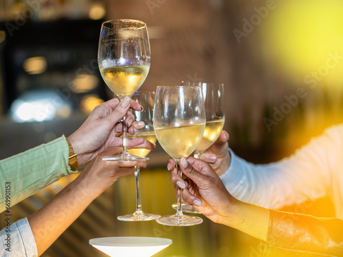 A close-up of friends raising their glasses in a toast  celebrating with chilled white wine. The golden hue from the ambiance emphasizes the warmth of the gathering.