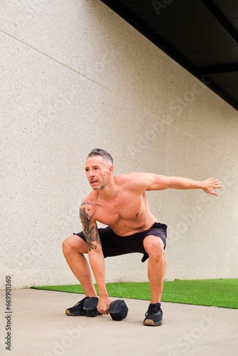 Fotografija Strong man doing dumbbell squat snatch in a outdoor fitness gym