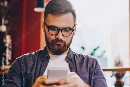 Serious male blogger in eyewear for vision correction reading sms with notification for app on smartphone