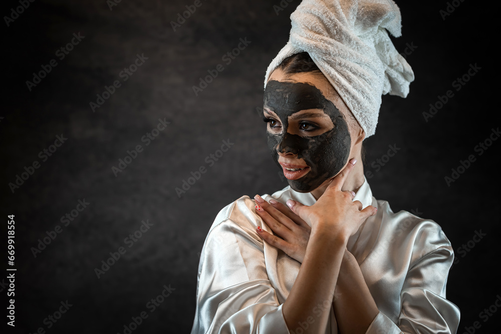 Beautiful young woman with black clay mask isolated on black