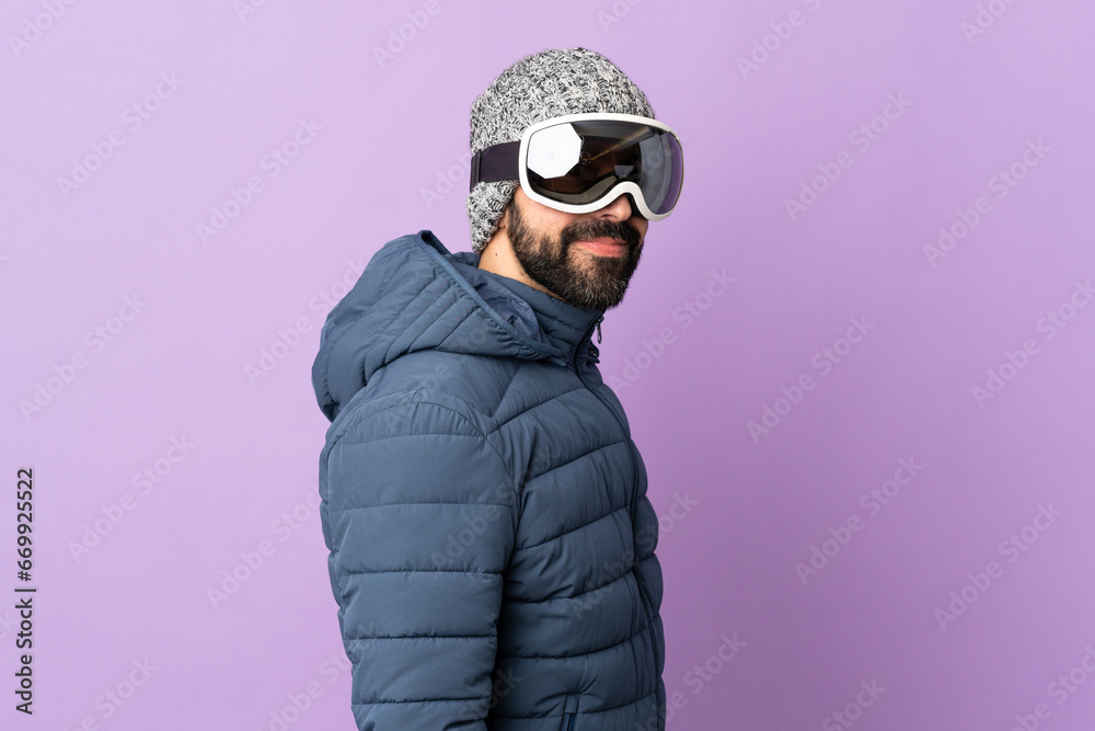 Skier man with snowboarding glasses over isolated purple background Skier man with snowboarding glasses over isolated purple background