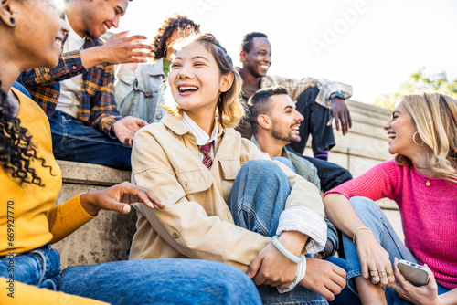Multicultural friends having fun laughing out loud in city street - Group of young people smiling outdoors - Friendship concept with guys and girls talking and socializing hanging out together © Davide Angelini