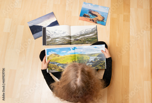 Child looking at the printed real paper travel photo books on home floor. Photographer has copyrights of the pictures in books, they are handmade. Photobook concept.
