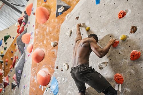 good looking fit african american man with his shirt off climbing up rock wall and looking down