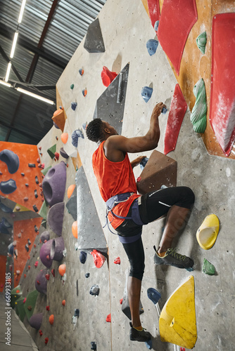 good looking african american male model ascending up rock bouldering wall with alpine harness