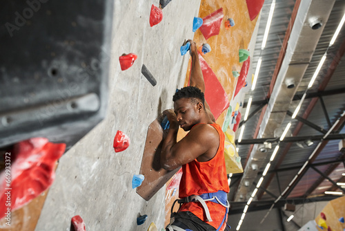 handsome young african american male model with alpine harness climbing up bouldering wall