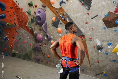 back view of young african american man with his hands akimbo standing next to climbing wall
