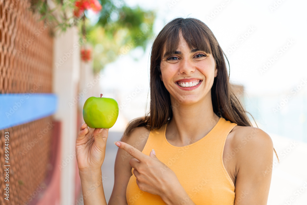 Young woman with an apple at outdoors and pointing it Young woman with an apple at outdoors and pointing it
