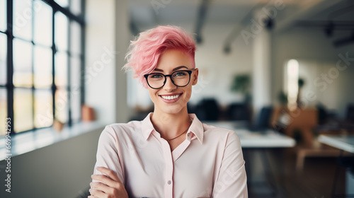 young happy artist woman with short pink hair wearing glasses and looking at the camera standing inside a working place photo