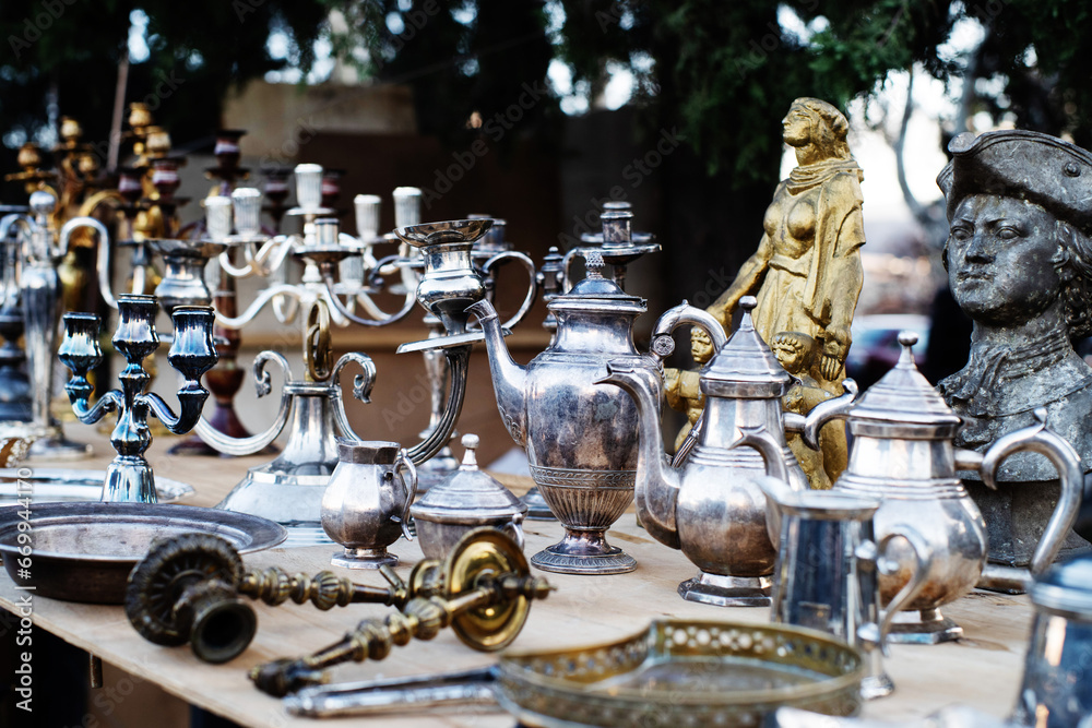 Fototapeta premium Vintage copper and metal antiques, tableware, jugs, trays, plates, figurines on a counter at a street flea market in Tbilisi. Antique dishes