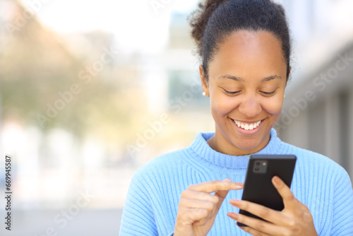 Happy black woman using cell phone in the street