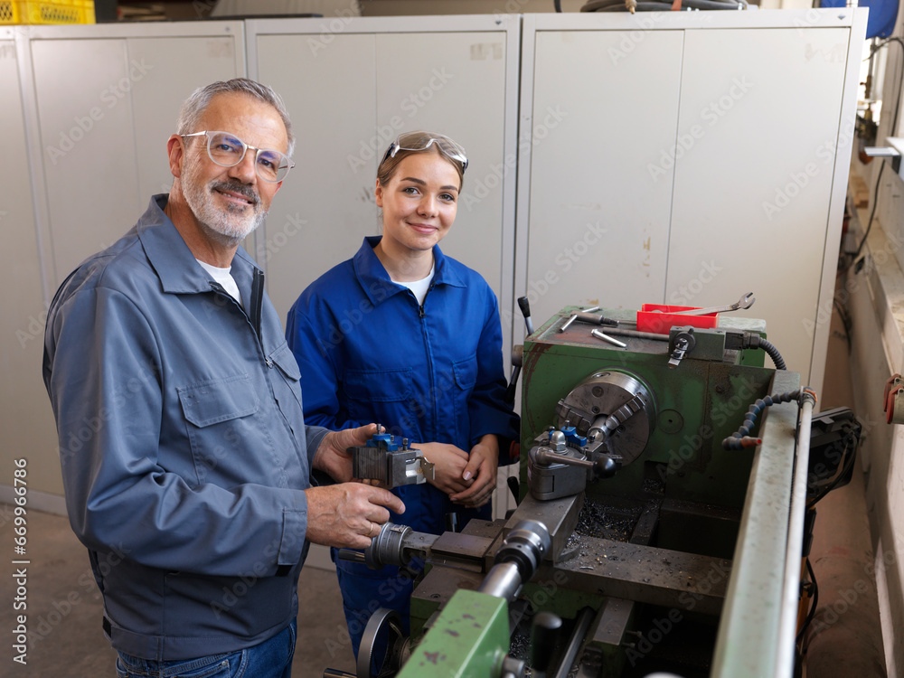 Smiling trainee standing with instructor near lathe machine at workshop Smiling trainee standing with instructor near lathe machine at workshop