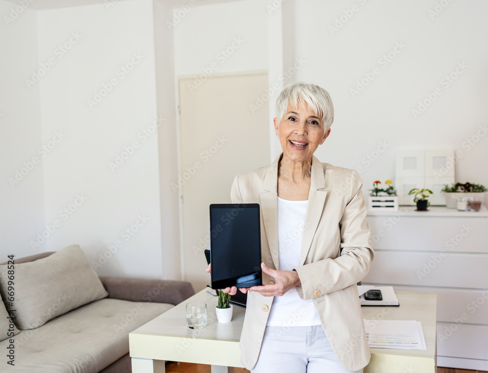 Shot of a mature beautiful businesswoman holding up a digital tablet with a white screen. Businesswoman with digital tablet in home office. Shot of a mature beautiful businesswoman holding up a digital tablet with a white screen. Businesswoman with digital tablet in home office.