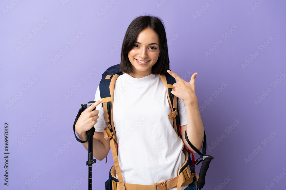 Young caucasian woman with backpack and trekking poles isolated on blue background giving a thumbs up gesture