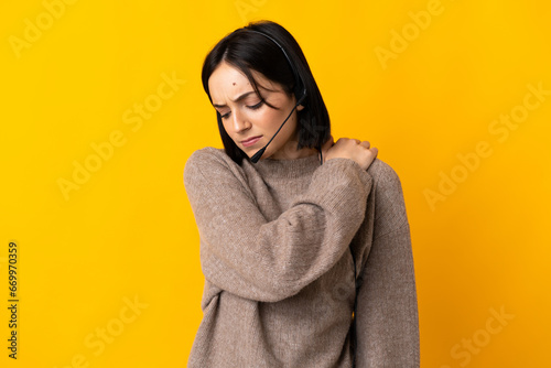 Young telemarketer woman isolated on yellow background suffering from pain in shoulder for having made an effort photo