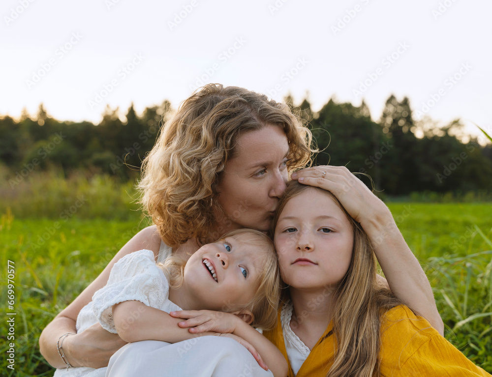 Mother kissing and embracing daughters in field Mother kissing and embracing daughters in field