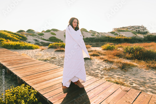 Woman wrapped in blanket standing on boardwalk at beach