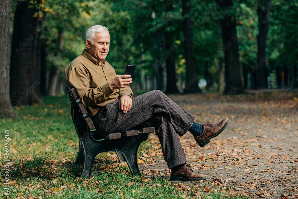 Senior man sitting on bench and using smart phone at autumn park Senior man sitting on bench and using smart phone at autumn park