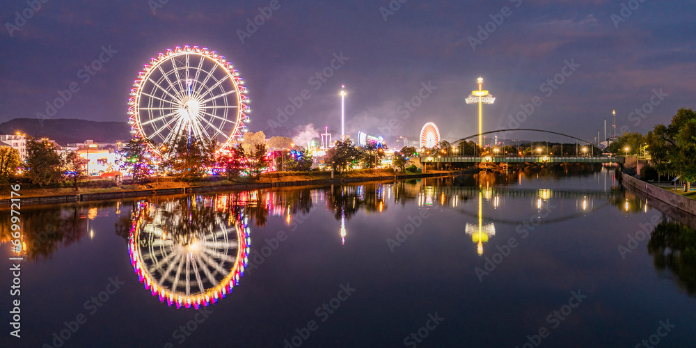 Germany, Baden-Wurttemberg, Stuttgart, Cannstatter Wasen, Panoramic view of glowing Ferris Wheel reflecting in Neckar river at night