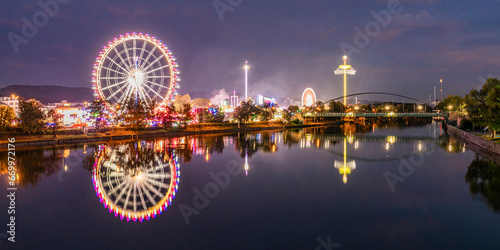 Germany, Baden-Wurttemberg, Stuttgart, Cannstatter Wasen, Panoramic view of glowing Ferris Wheel reflecting in Neckar river at night photo