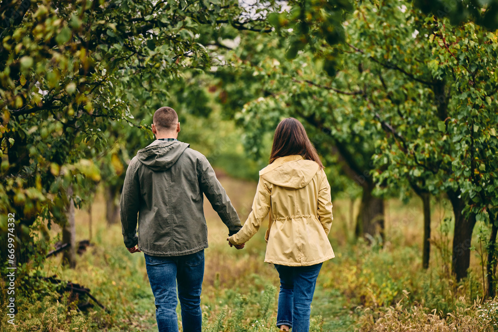 Two lovers enjoying nature, walking through the orchard, holding hands.