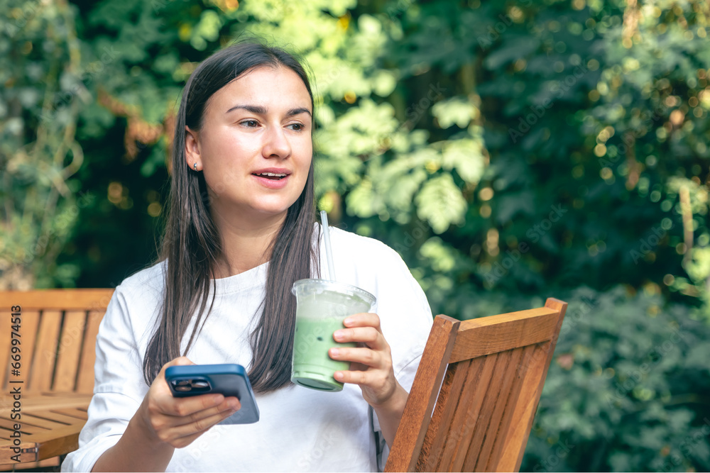A woman drinking matcha latte coffee and using smartphone in a cafe A woman drinking matcha latte coffee and using smartphone in a cafe