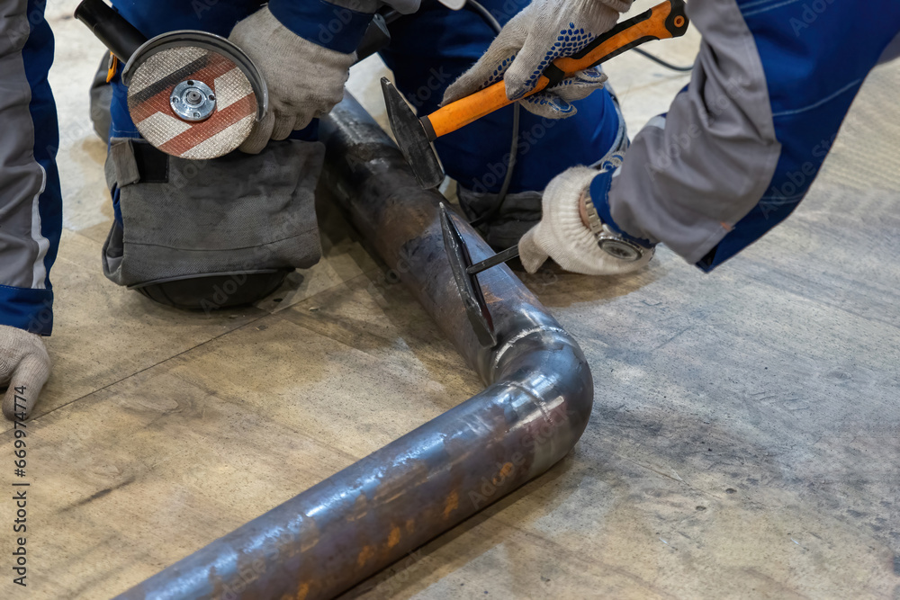 Processing seam on pipe after welding. Two craftsmen are repairing pipeline. Cropped workers are