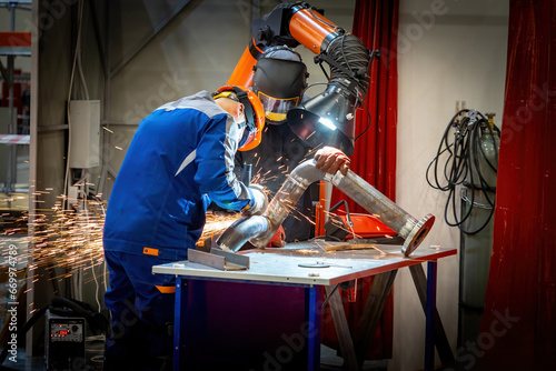 Man workers are repairing fragment pipeline. Craftsmen work in production factory. Guys use grinding machine. Sanding weld seam on pipe. Repair pipeline at factory. Workers near table for welding