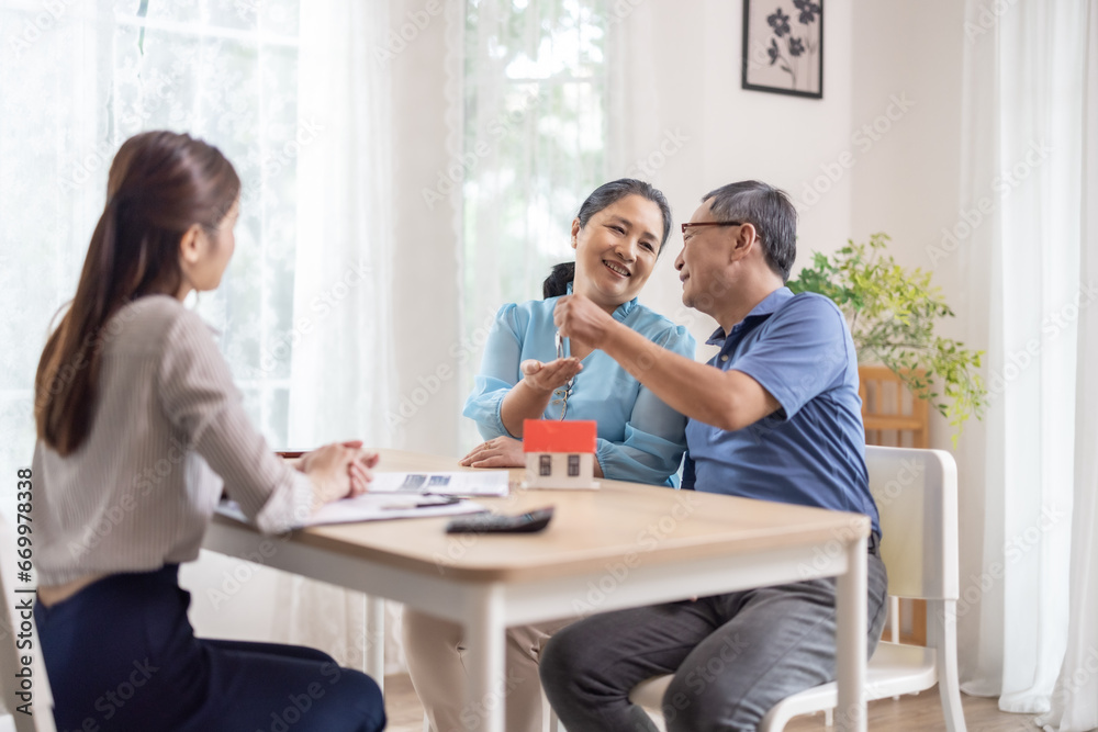 Elderly couples satisfying retirement home purchase with contract and key handover from a saleswoman Elderly couples satisfying retirement home purchase with contract and key handover from a saleswoman