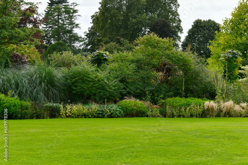 Scenic view of a beautiful English style landscape garden with a green mowed grass lawn and a colourful flower bed