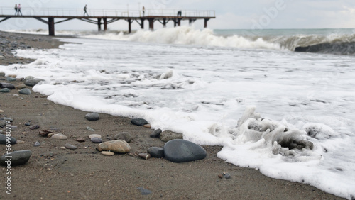Pebbles lie on the sandy sea beach. Foamy waves roll in. selective focus