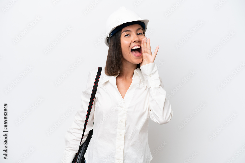 Young architect woman with helmet and holding blueprints isolated on white background shouting with mouth wide open Young architect woman with helmet and holding blueprints isolated on white background shouting with mouth wide open