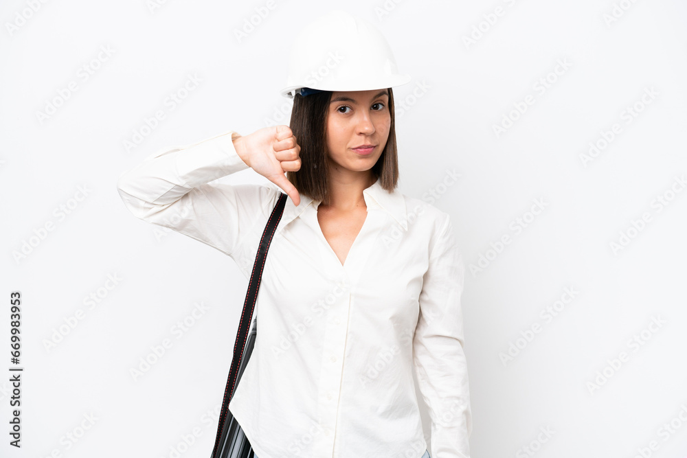 Young architect woman with helmet and holding blueprints isolated on white background showing thumb down with negative expression Young architect woman with helmet and holding blueprints isolated on white background showing thumb down with negative expression