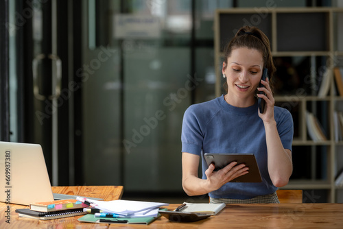Businesswoman talking on the phone with friend or colleague while checking documents in modern office